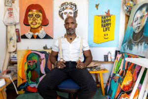 black main in white shirt black pants and suspenders sitting in chair in front of art